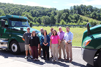 Representatives from Haywood Builders and Haywood Community College standing between two semi trucks with the mountains in the background
